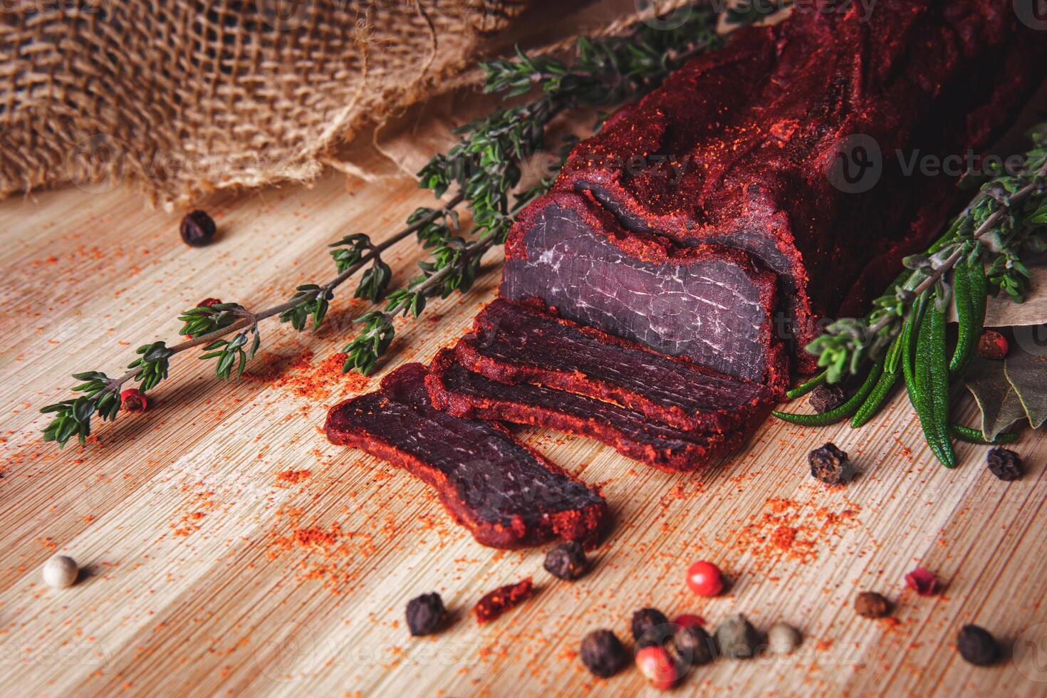 Close-up of basturma sliced into pieces. Dried meat with spices cut into slices. Dried horse meat on a wooden board with rosemary and caraway herbs photo