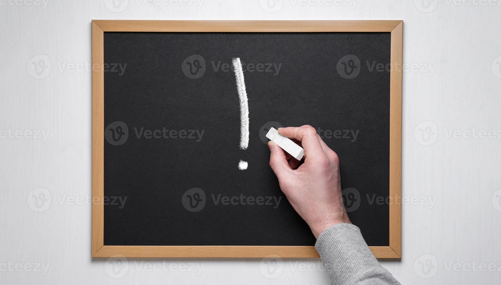 Hand holding chalk on blackboard.Exclamation point on a chalk board. photo