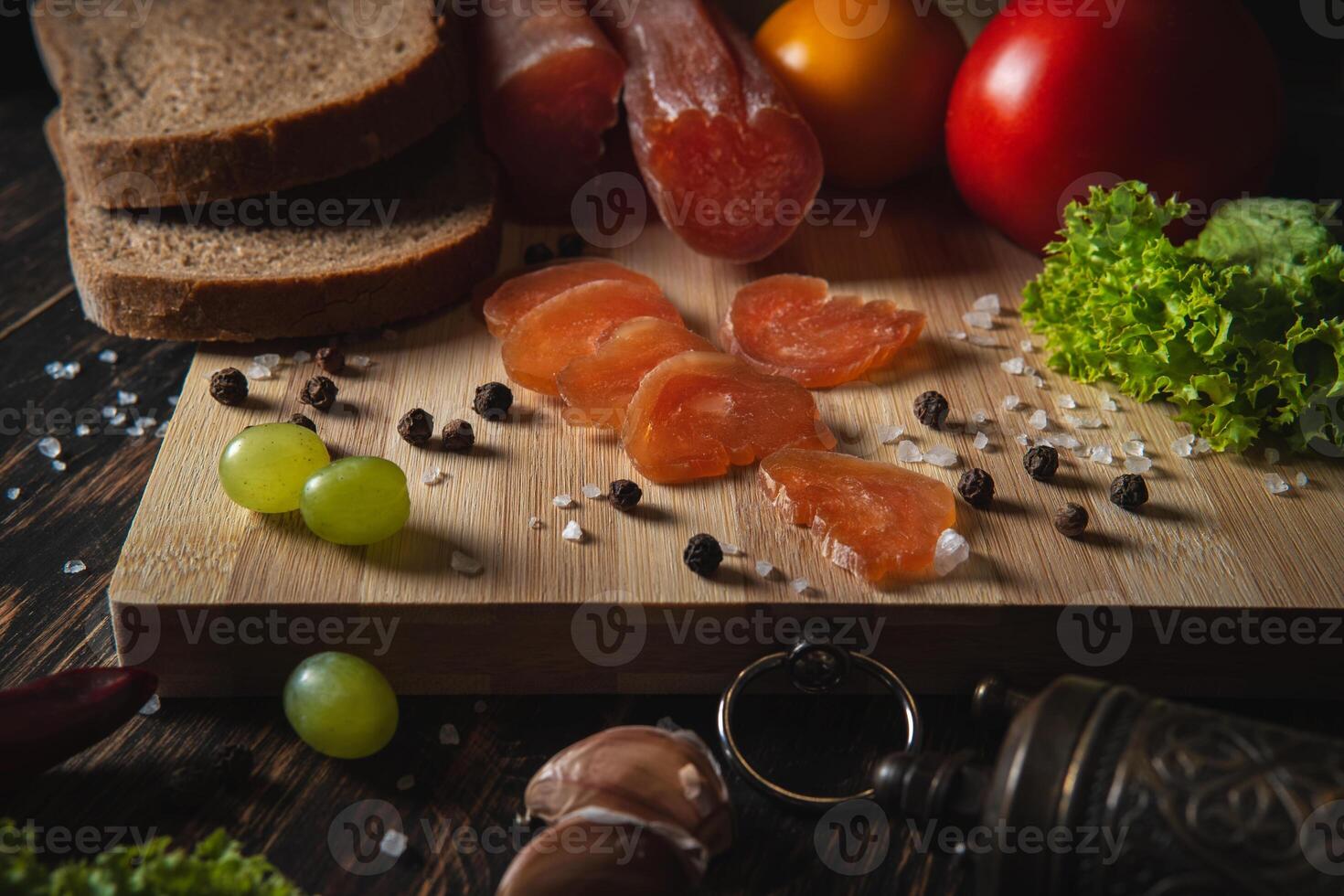 Sliced jerky on a board. Vegetables, bread and meat on the table. photo