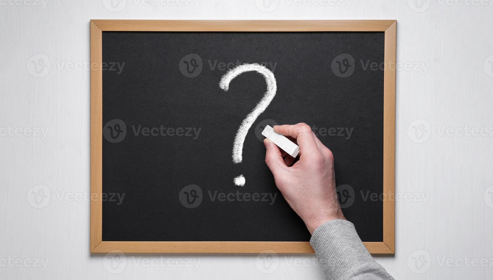 Male hand draws a question mark on the blackboard with chalk. The question mark is depicted on a chalk board. photo