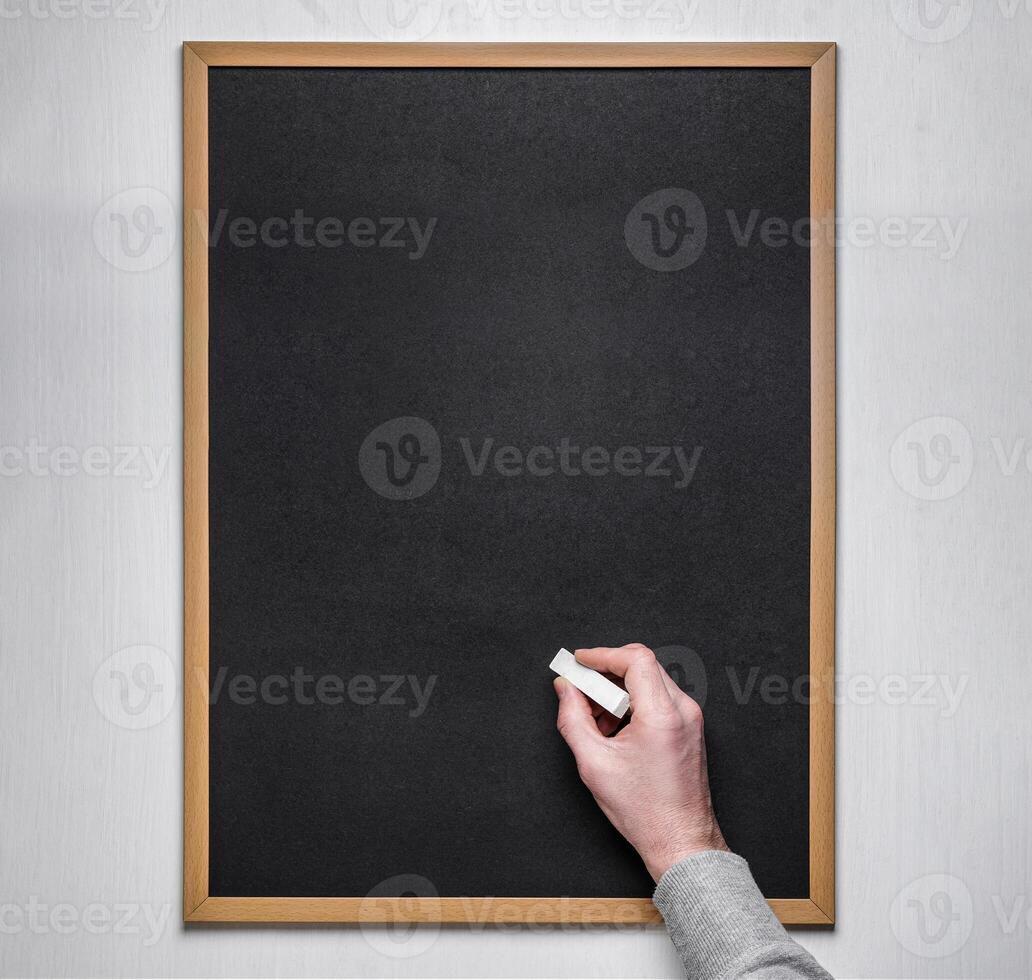 Male hand with chalk on the empty blackboard or chalkboard. photo
