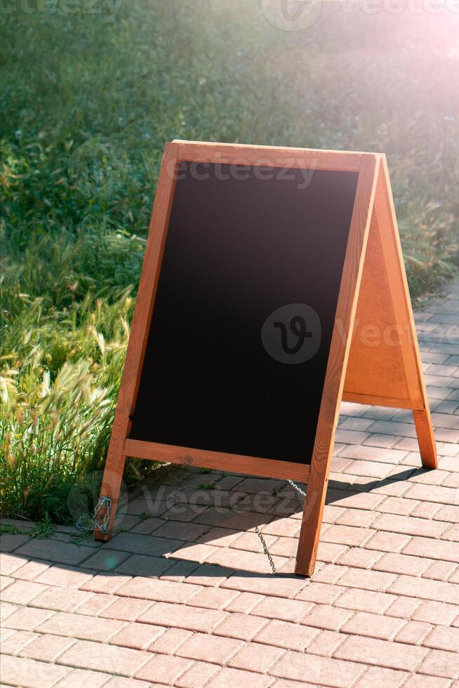 A black chalkboard stand on wood for a restaurant menu in the street. Empty menu board on street. Empty menu board on street on the pub or restaurant background. Beauty and minimalism style photo