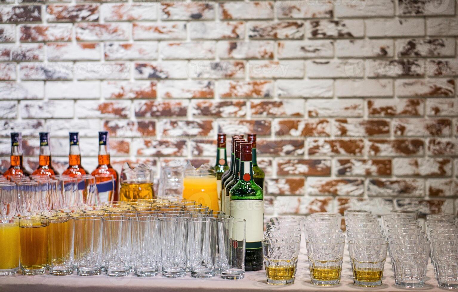 Empty and filled glasses next to bottles of alcoholic beverages on a brick wall background. Banquet or party preparations. photo