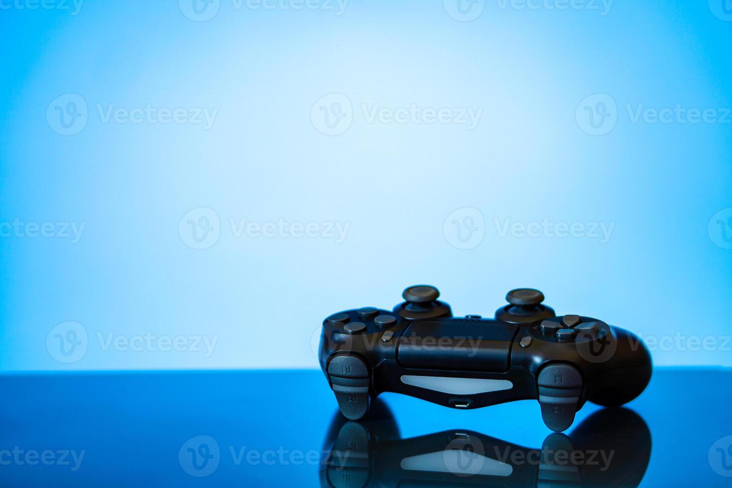 modern black gamepad on a glossy surface and a glowing blue photo