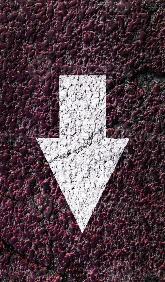 White pointing arrow on a textured asphalt surface. photo