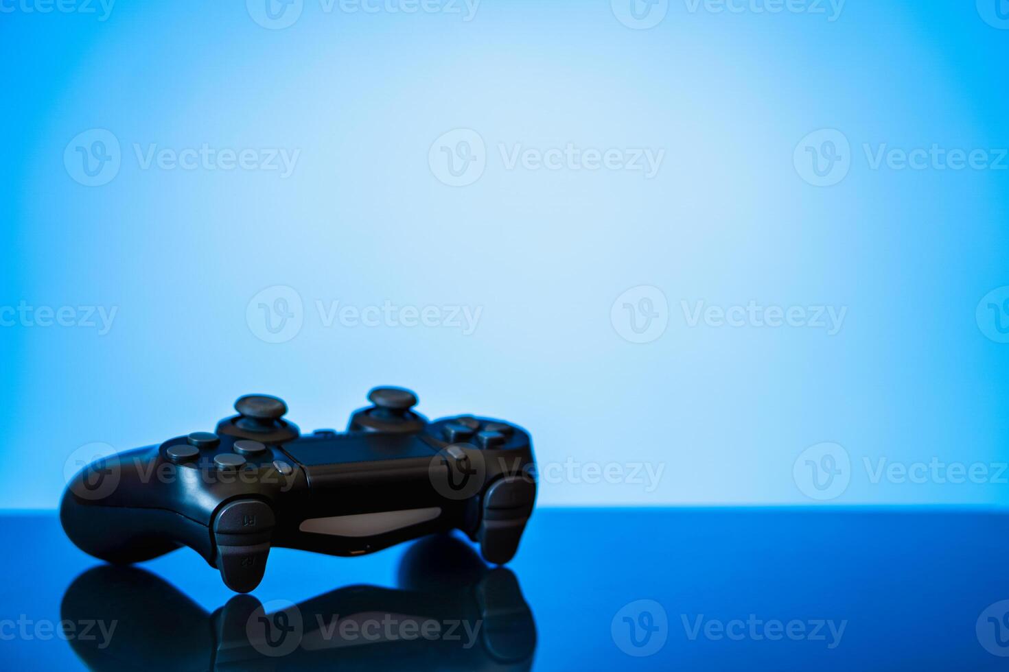 modern black gamepad on a glossy surface and a glowing blue photo