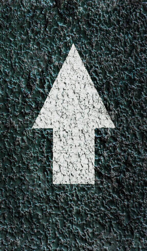 White pointing arrow on a textured asphalt surface. photo