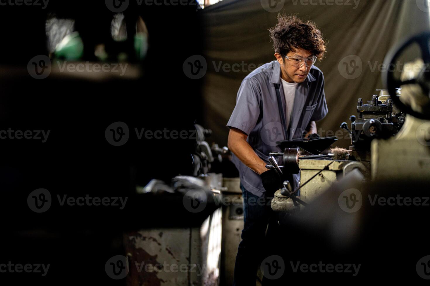 Asian worker in production plant drilling at machine. Professional worker near drilling machine on factory. finishing metal working internal steel surface on lathe grinder machine with flying sparks. photo