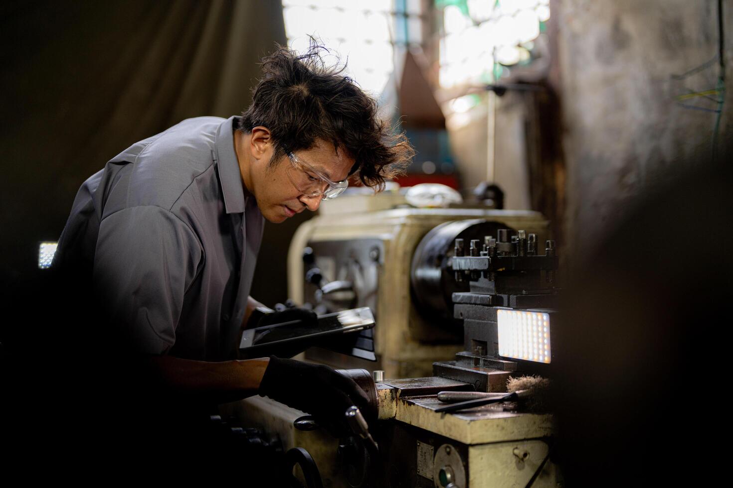 Asian worker in production plant drilling at machine. Professional worker near drilling machine on factory. finishing metal working internal steel surface on lathe grinder machine with flying sparks. photo