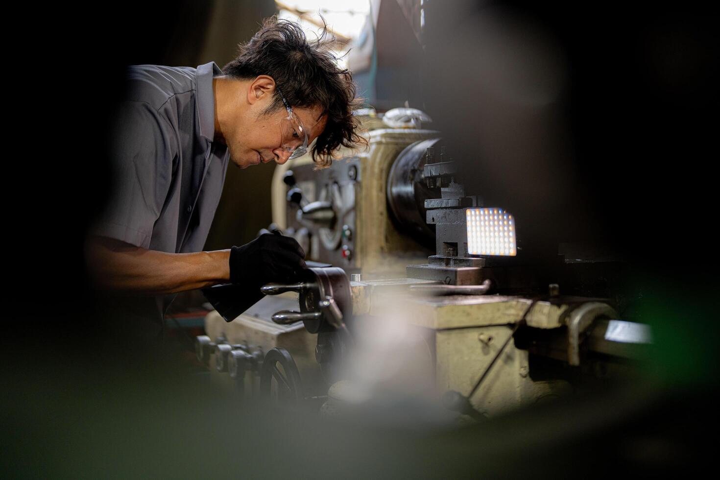 Asian worker in production plant drilling at machine. Professional worker near drilling machine on factory. finishing metal working internal steel surface on lathe grinder machine with flying sparks. photo