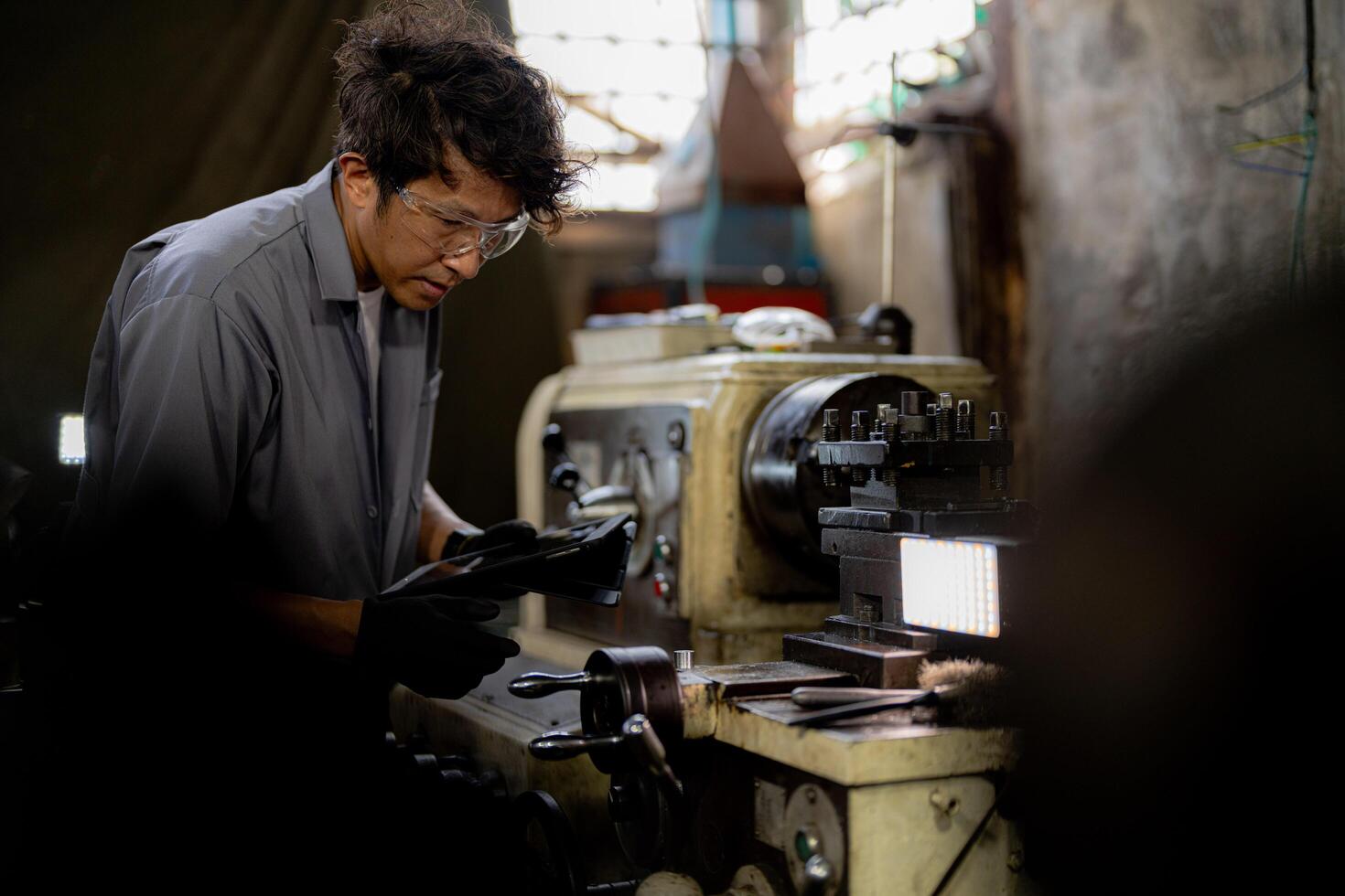 Asian worker in production plant drilling at machine. Professional worker near drilling machine on factory. finishing metal working internal steel surface on lathe grinder machine with flying sparks. photo