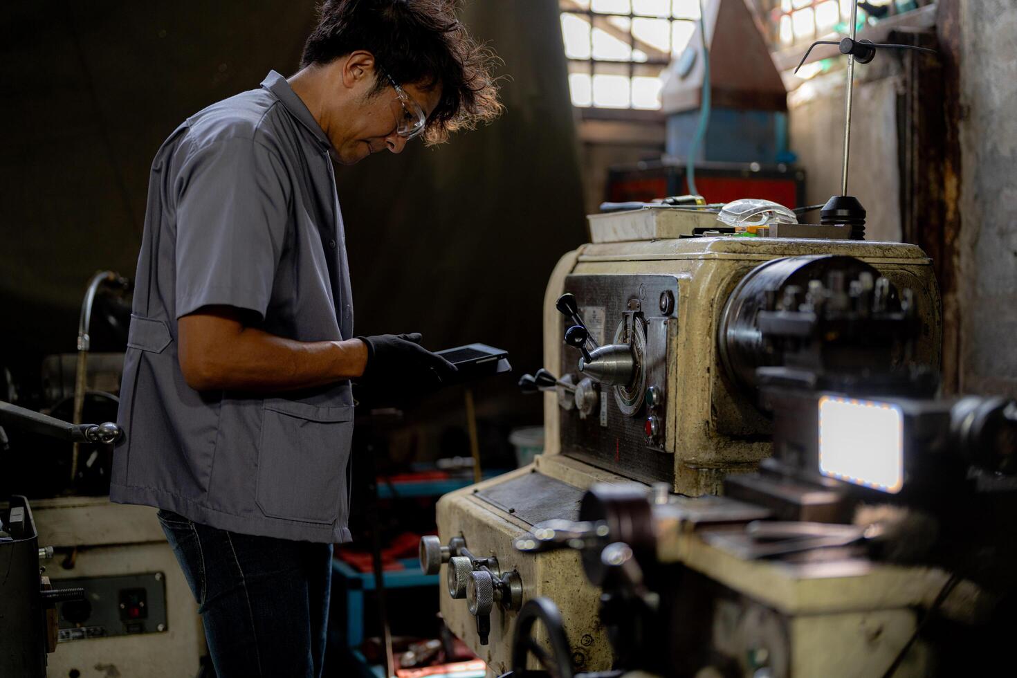 Asian worker in production plant drilling at machine. Professional worker near drilling machine on factory. finishing metal working internal steel surface on lathe grinder machine with flying sparks. photo