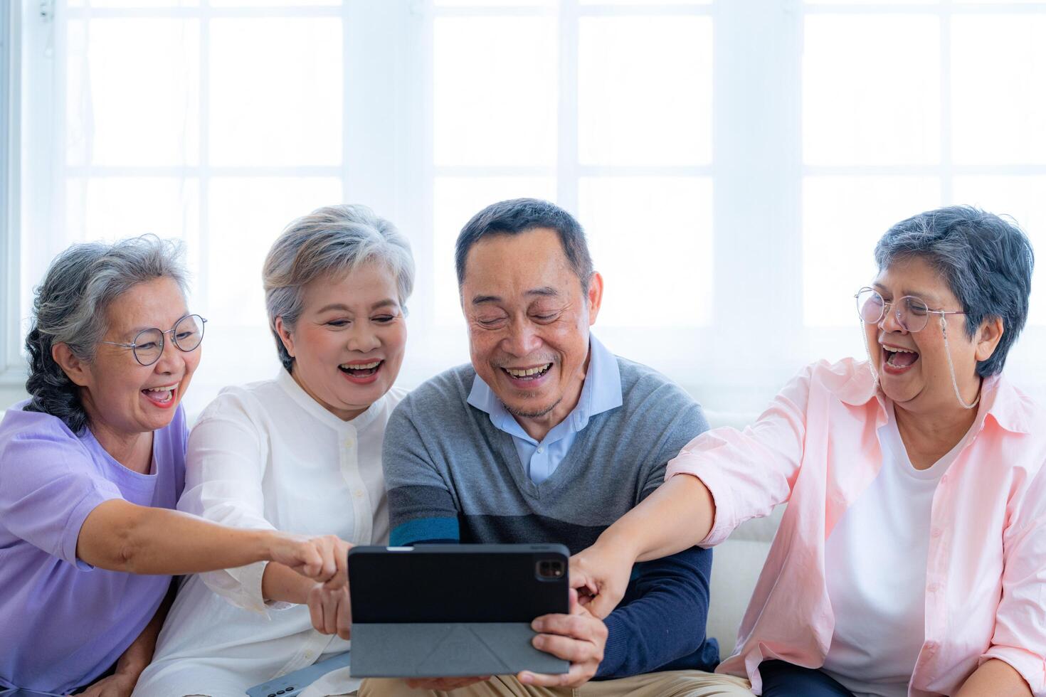 Happiness of the group females and male elderly talking with Call from smart tablet. Senior people are talking and enjoy together at the living room. Joyful retired friends enjoying relaxation. photo