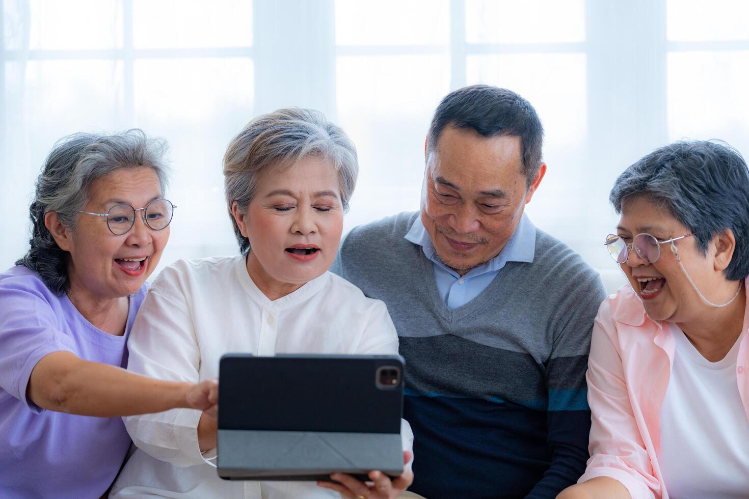 Happiness of the group females and male elderly talking with Call from smart tablet. Senior people are talking and enjoy together at the living room. Joyful retired friends enjoying relaxation. photo