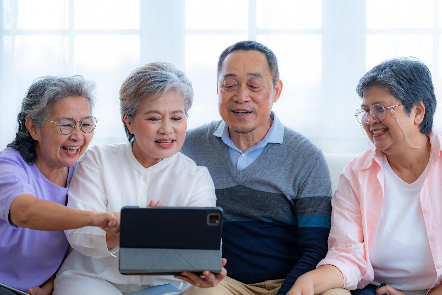 Happiness of the group females and male elderly talking with Call from smart tablet. Senior people are talking and enjoy together at the living room. Joyful retired friends enjoying relaxation. photo