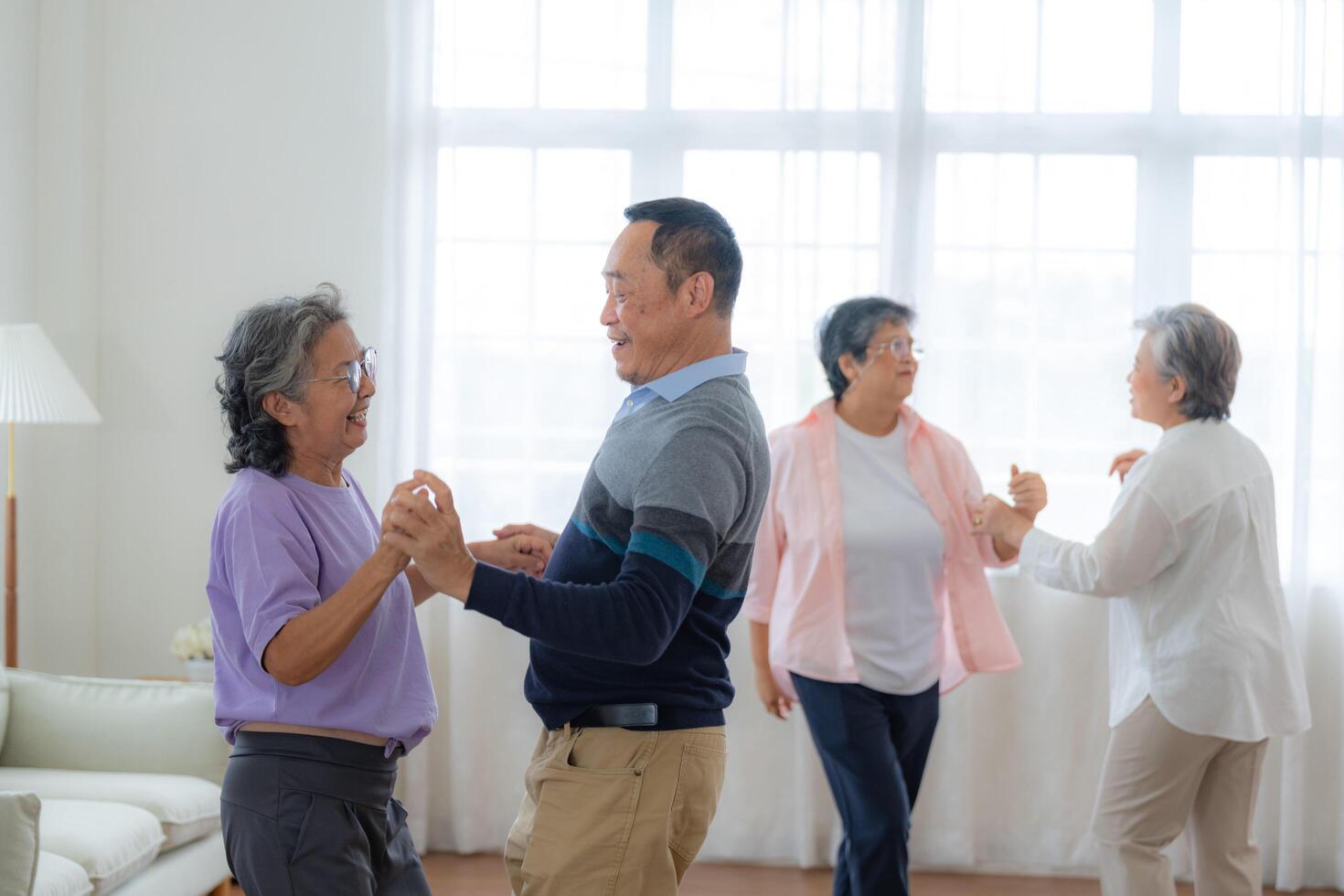 Asian Older male and females people dance with their partners on a dancing floor in living space. Happy older couple performing get exercise. Joyful carefree retired senior friends enjoying relaxation photo