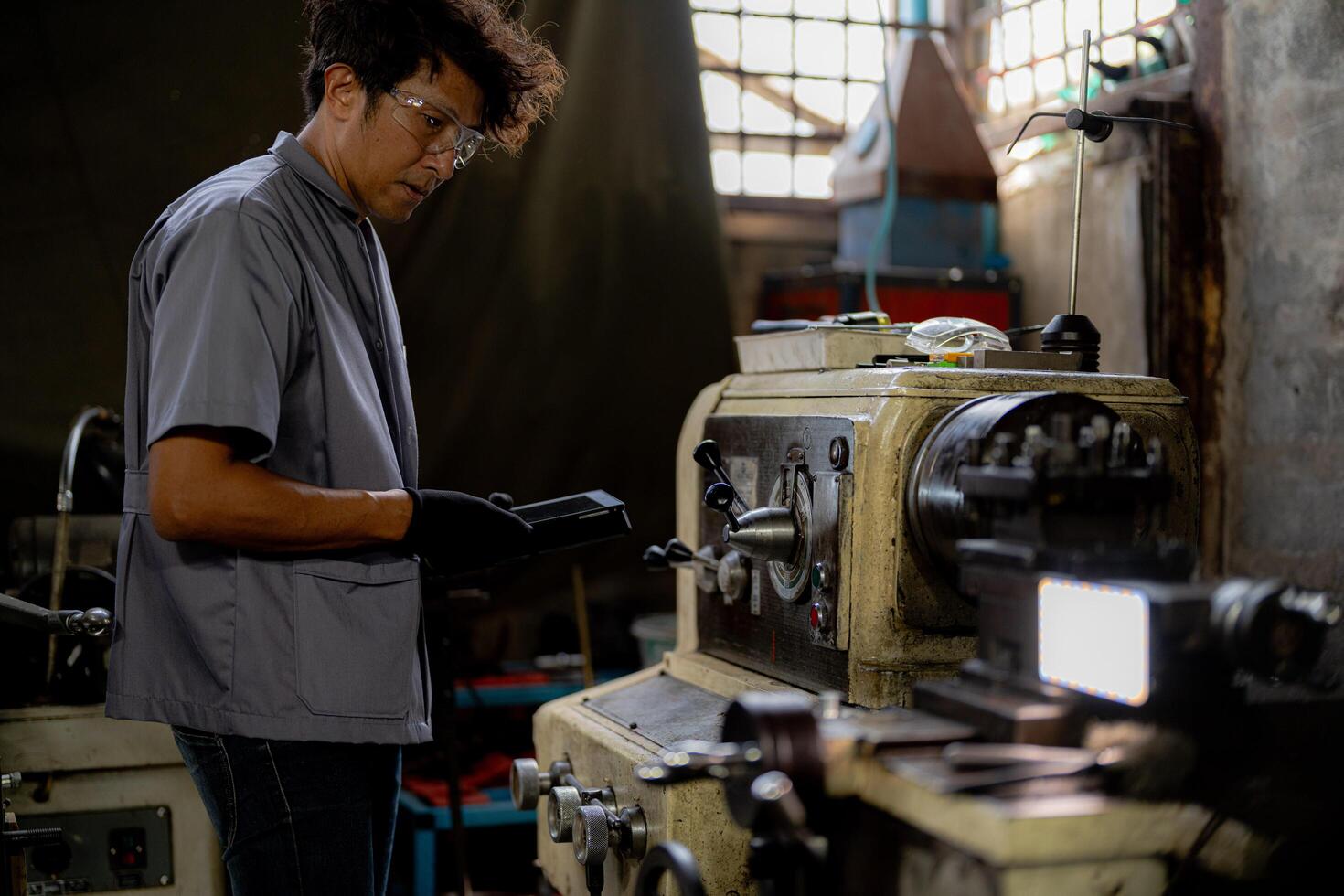 Asian worker in production plant drilling at machine. Professional worker near drilling machine on factory. finishing metal working internal steel surface on lathe grinder machine with flying sparks. photo