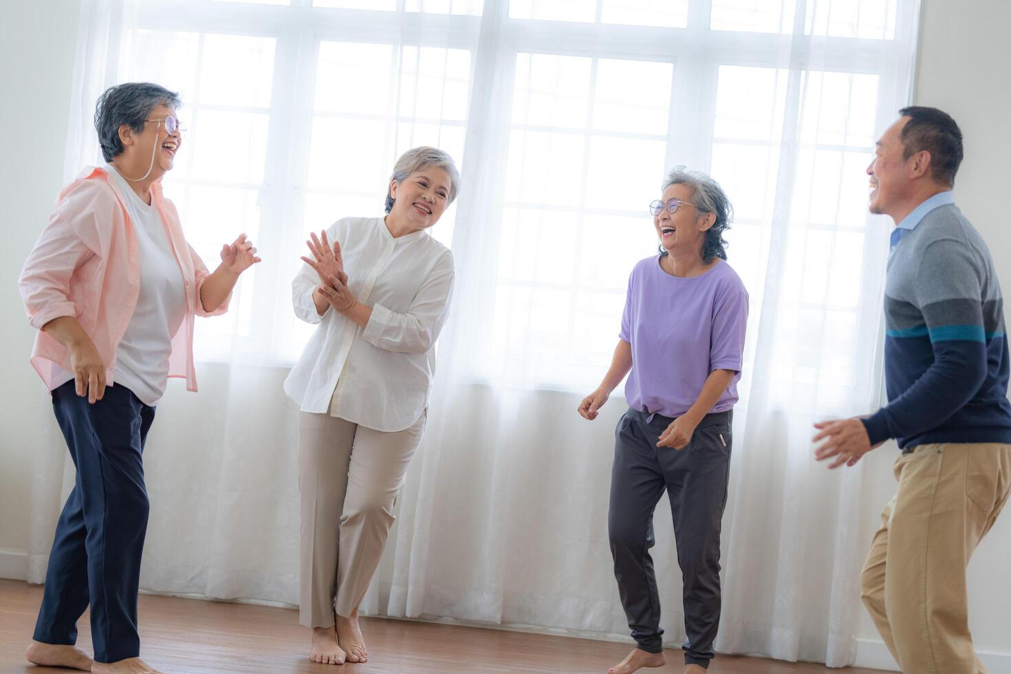 Asian Older male and females people dance with their partners on a dancing floor in living space. Happy older couple performing get exercise. Joyful carefree retired senior friends enjoying relaxation photo