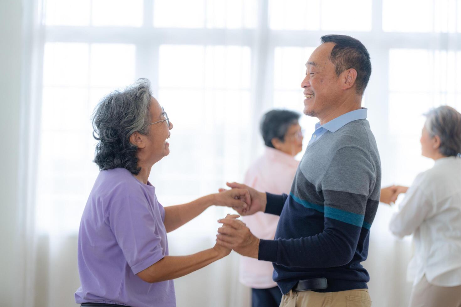 Asian Older male and females people dance with their partners on a dancing floor in living space. Happy older couple performing get exercise. Joyful carefree retired senior friends enjoying relaxation photo