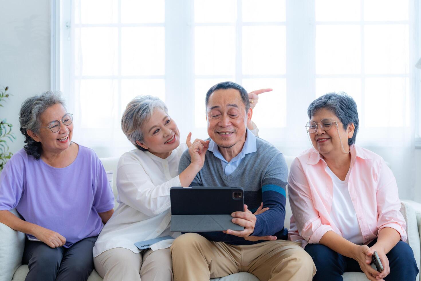 Happiness of the group females and male elderly talking with Call from smart tablet. Senior people are talking and enjoy together at the living room. Joyful retired friends enjoying relaxation. photo