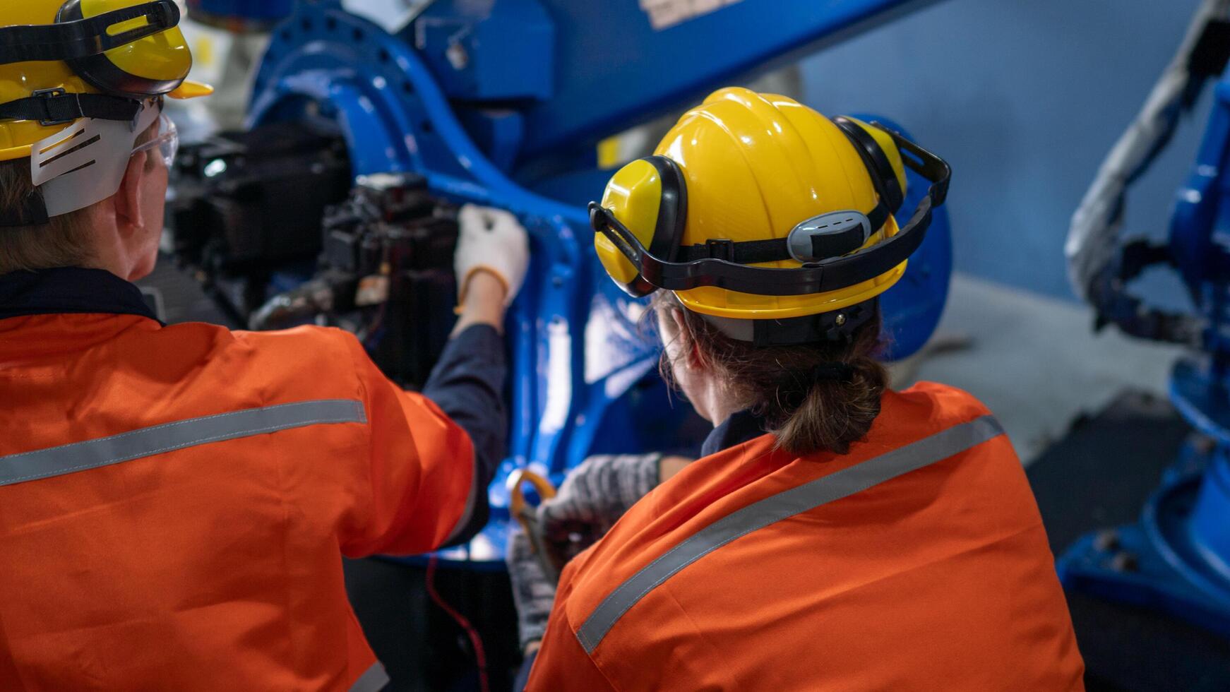 group of male engineer workers maintenance automatic robotic arm machine in a dark room factory. worker checking and repairing automatic robot hand machine. Worker wearing safety glasses and helmet. photo