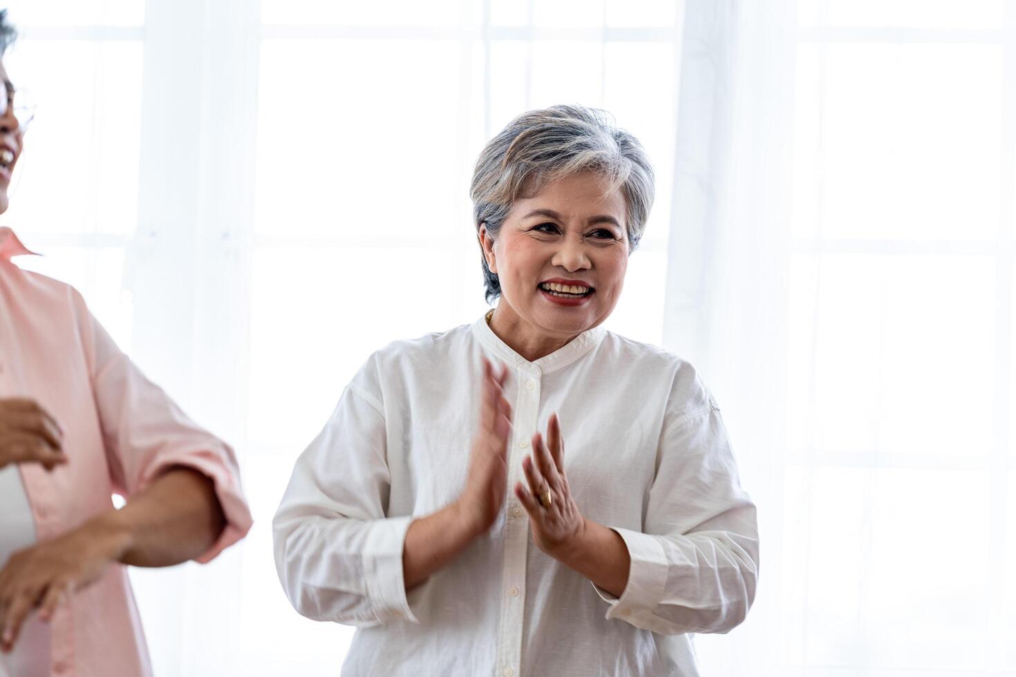 Asian Older male and females people dance with their partners on a dancing floor in living space. Happy older couple performing get exercise. Joyful carefree retired senior friends enjoying relaxation photo