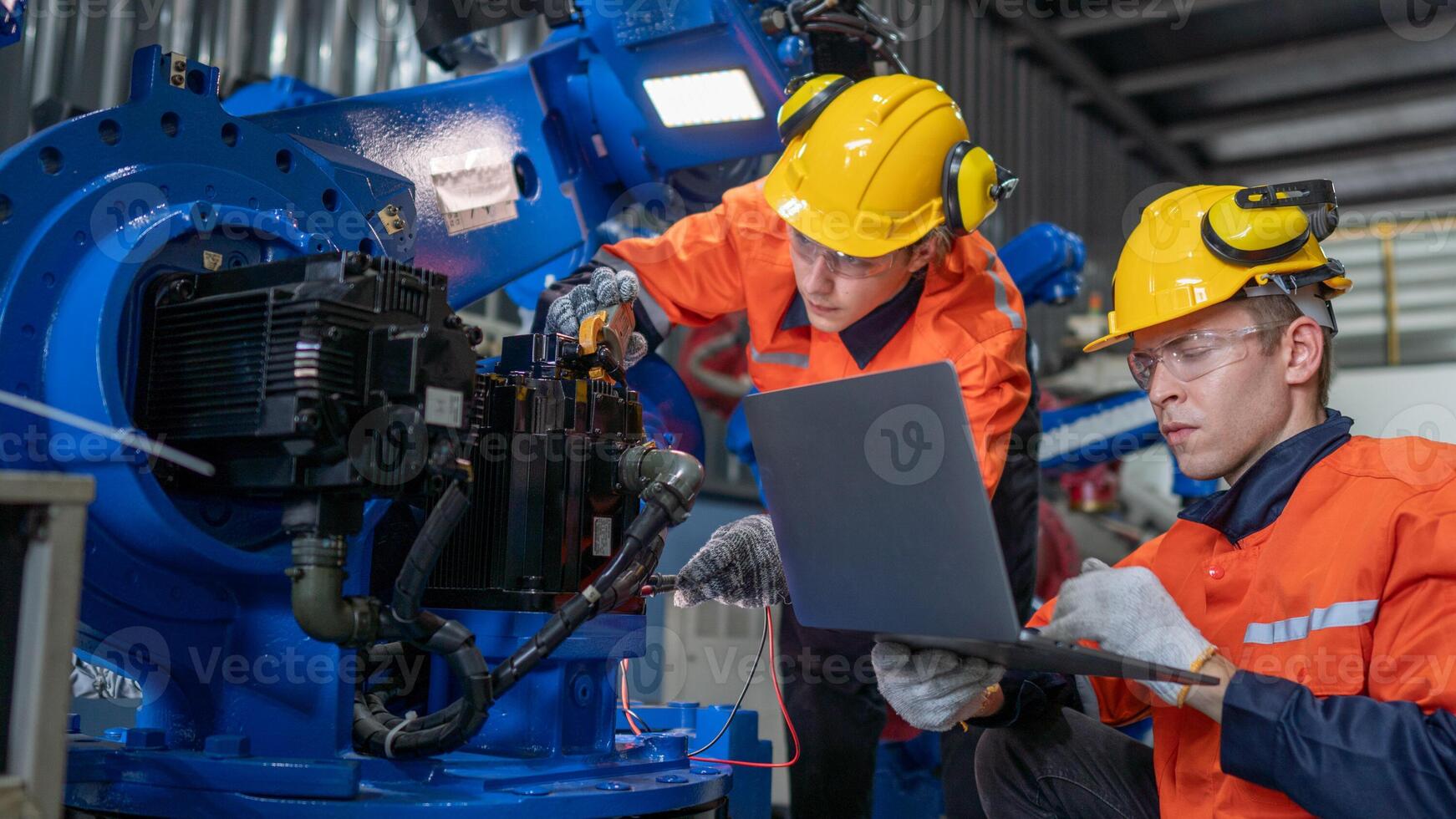 group of male engineer workers maintenance automatic robotic arm machine in a dark room factory. worker checking and repairing automatic robot hand machine. Worker wearing safety glasses and helmet. photo