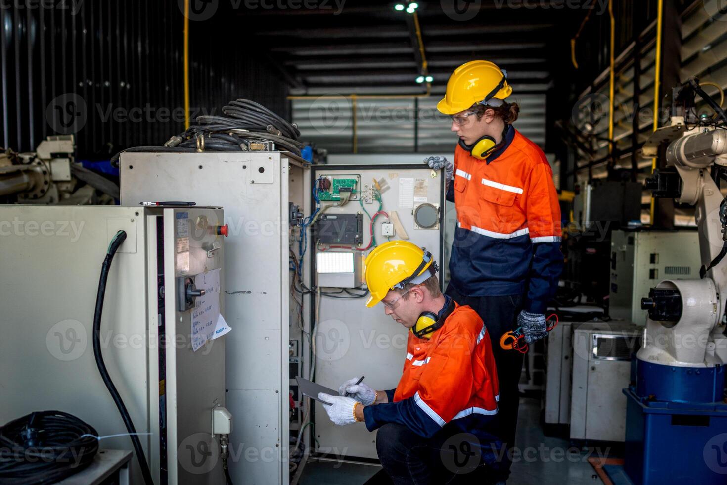 group of male engineer workers maintenance automatic robotic arm machine in a dark room factory. worker checking and repairing automatic robot hand machine. Worker wearing safety glasses and helmet. photo