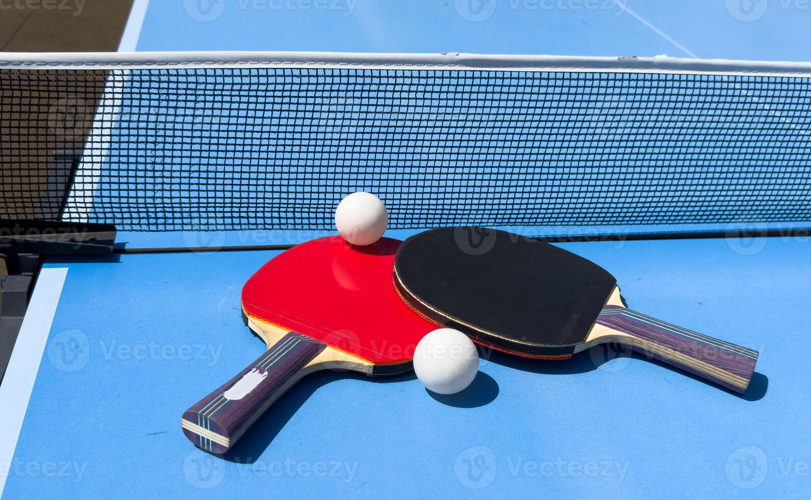 Two table tennis rackets and balls on a blue table with net. photo