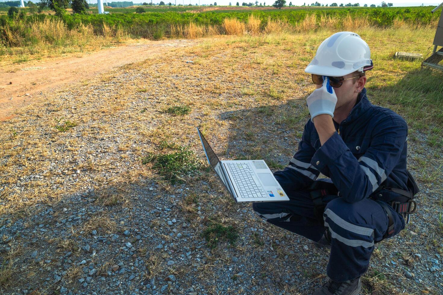 A technician in safety gear meticulously records data with a wind turbine in the backdrop at dusk. photo