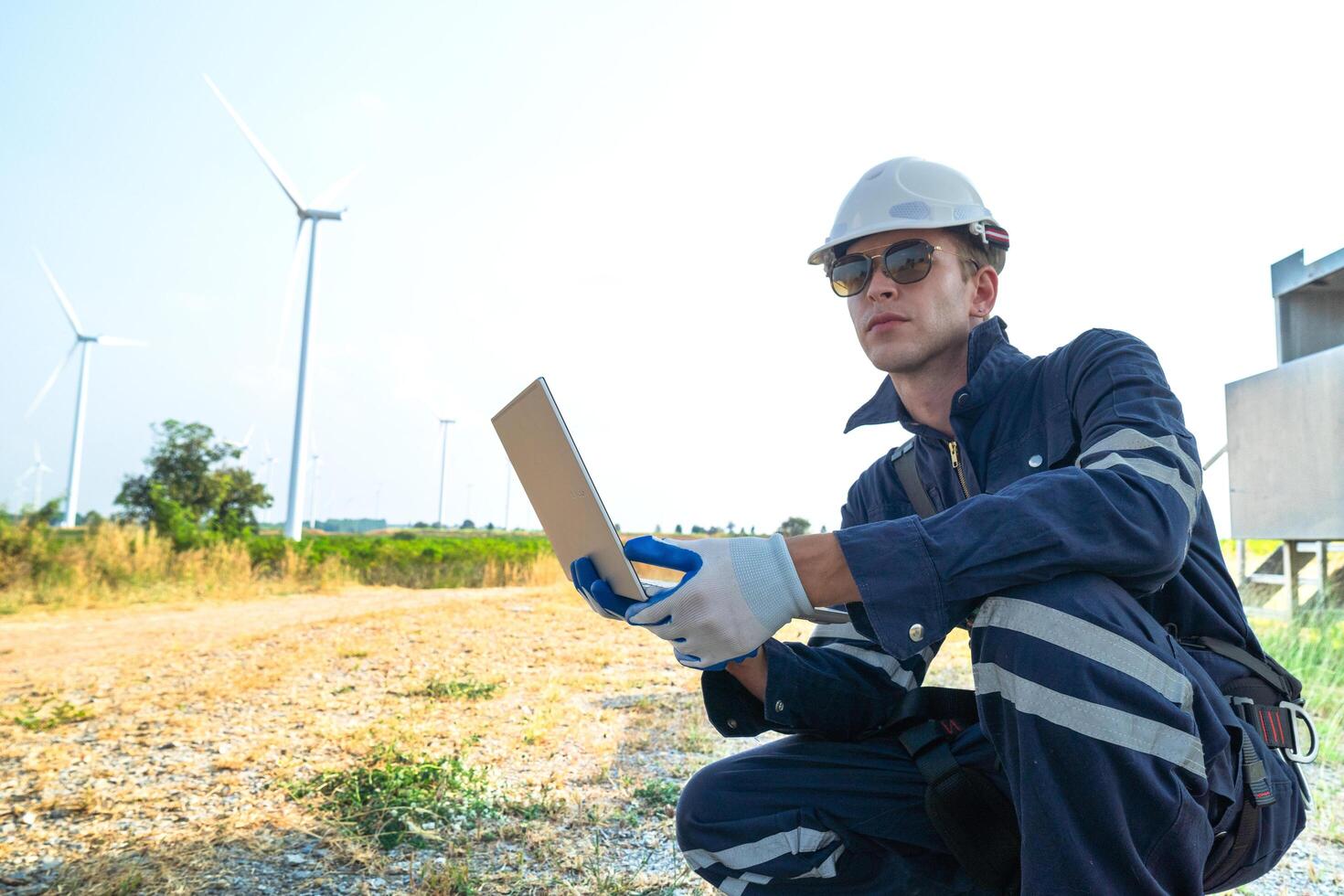 A technician in safety gear meticulously records data with a wind turbine in the backdrop at dusk. photo
