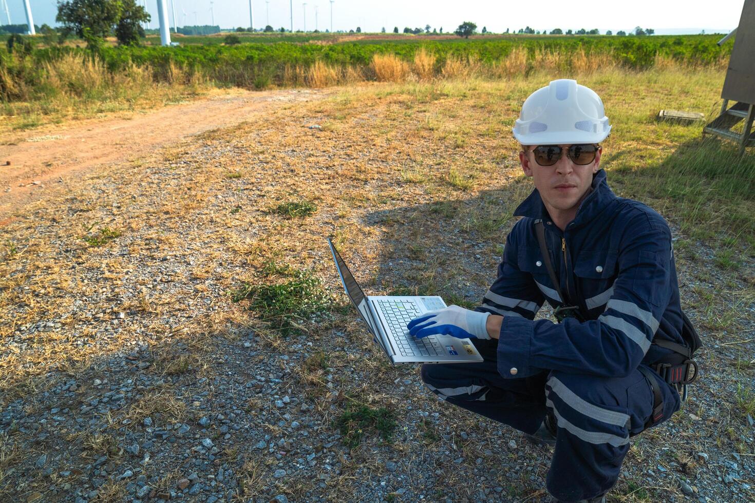 A technician in safety gear meticulously records data with a wind turbine in the backdrop at dusk. photo