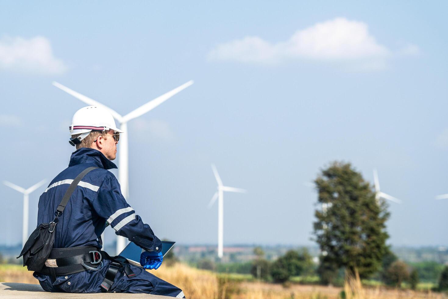 A wind energy technician with a laptop analyzes the efficiency of turbines on a clear day. photo