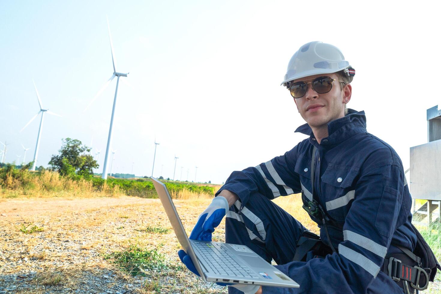 A technician in safety gear meticulously records data with a wind turbine in the backdrop at dusk. photo