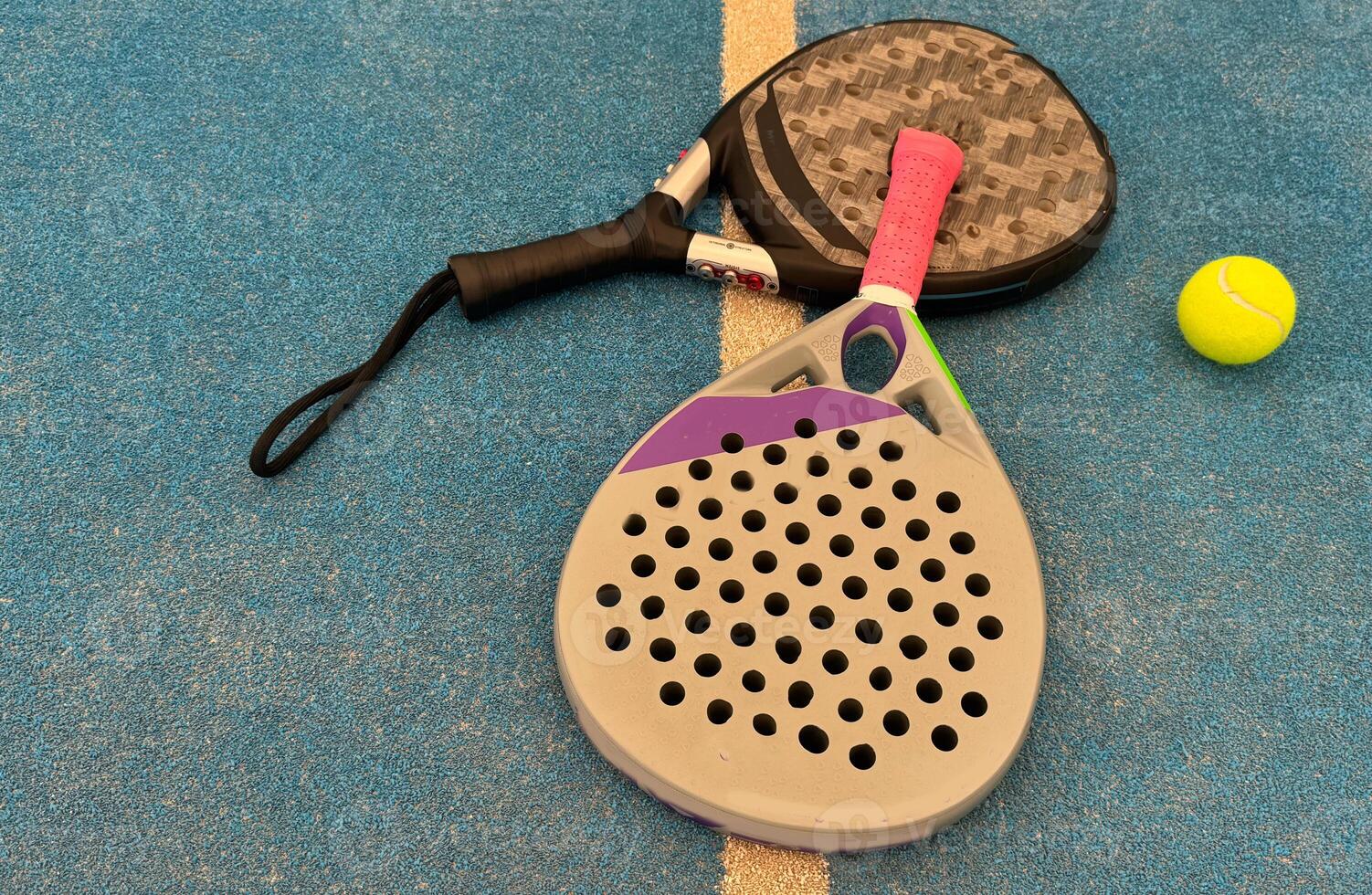 A padel tennis racket is laying on the ground next to a tennis ball on a padel court photo