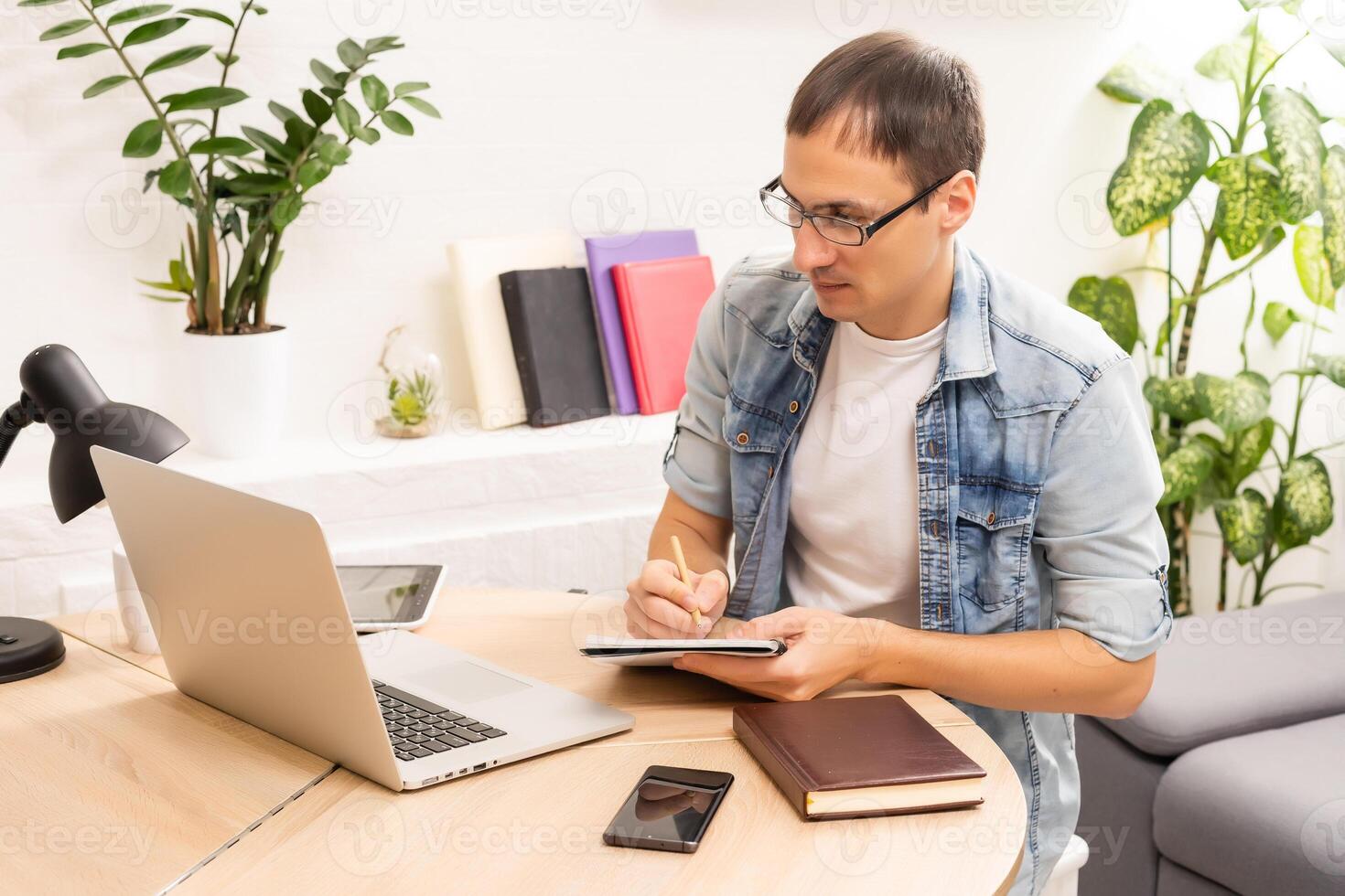 Happy young man, wearing glasses and smiling, as he works on his laptop to get all his business done early in the morning with his cup of coffee photo