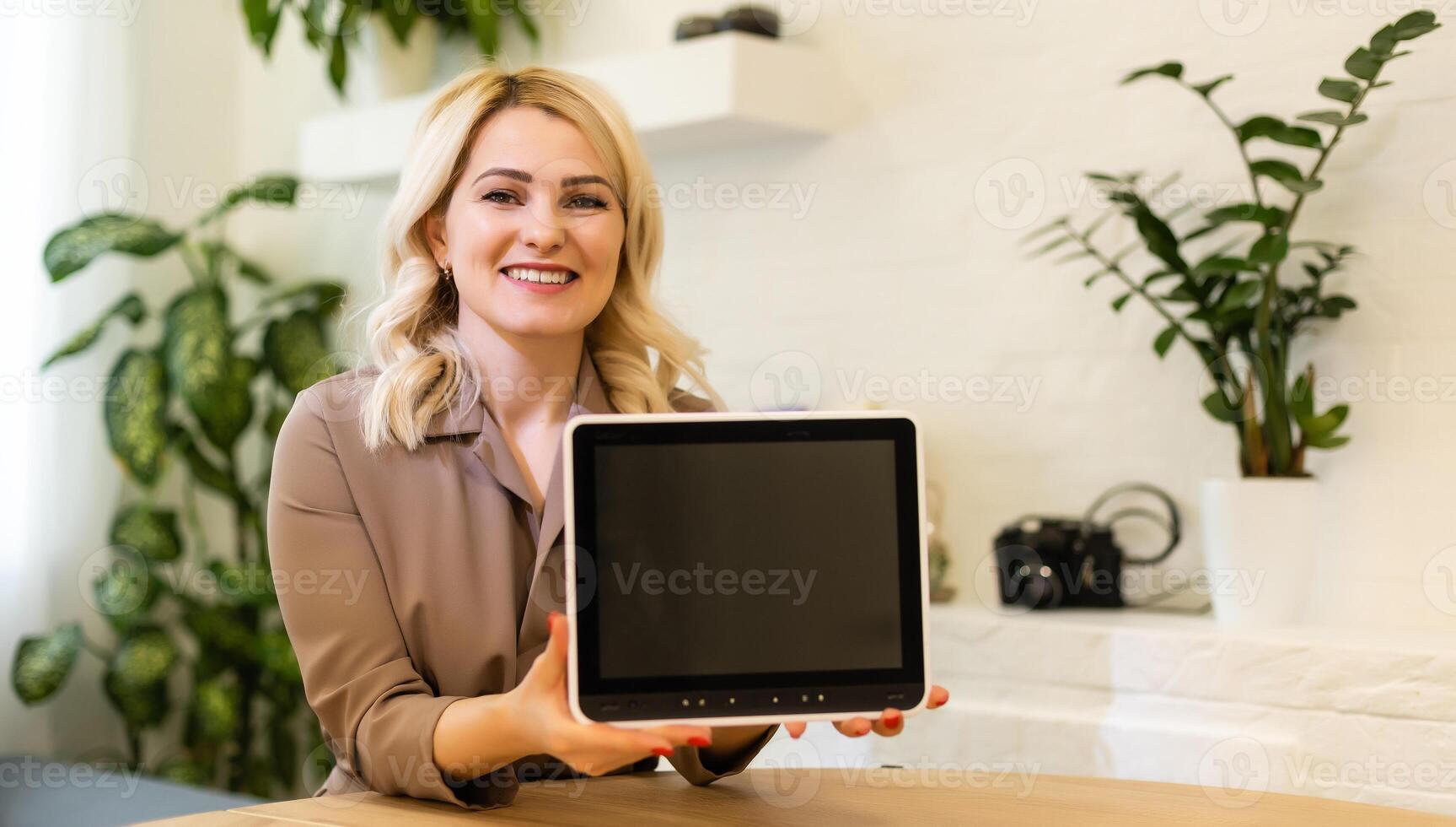 Young smiling woman showing blank tablet computer screen in office. Focus on tablet computer photo