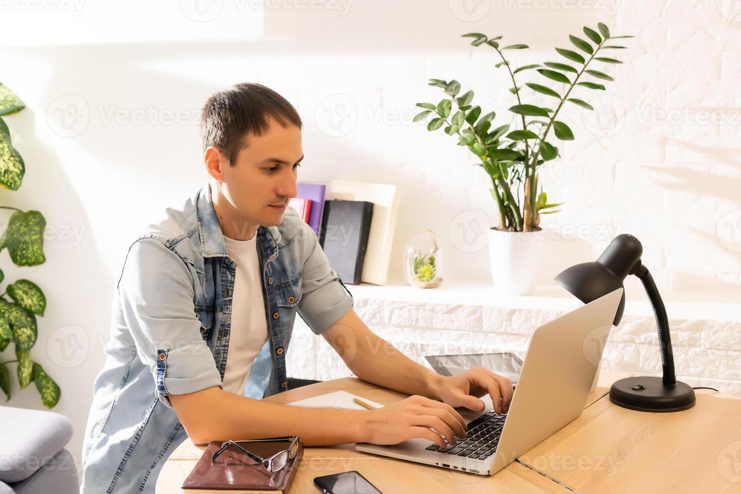 Happy young man smiling, as he works on his laptop to get all his business done early in the morning with his cup of coffee photo