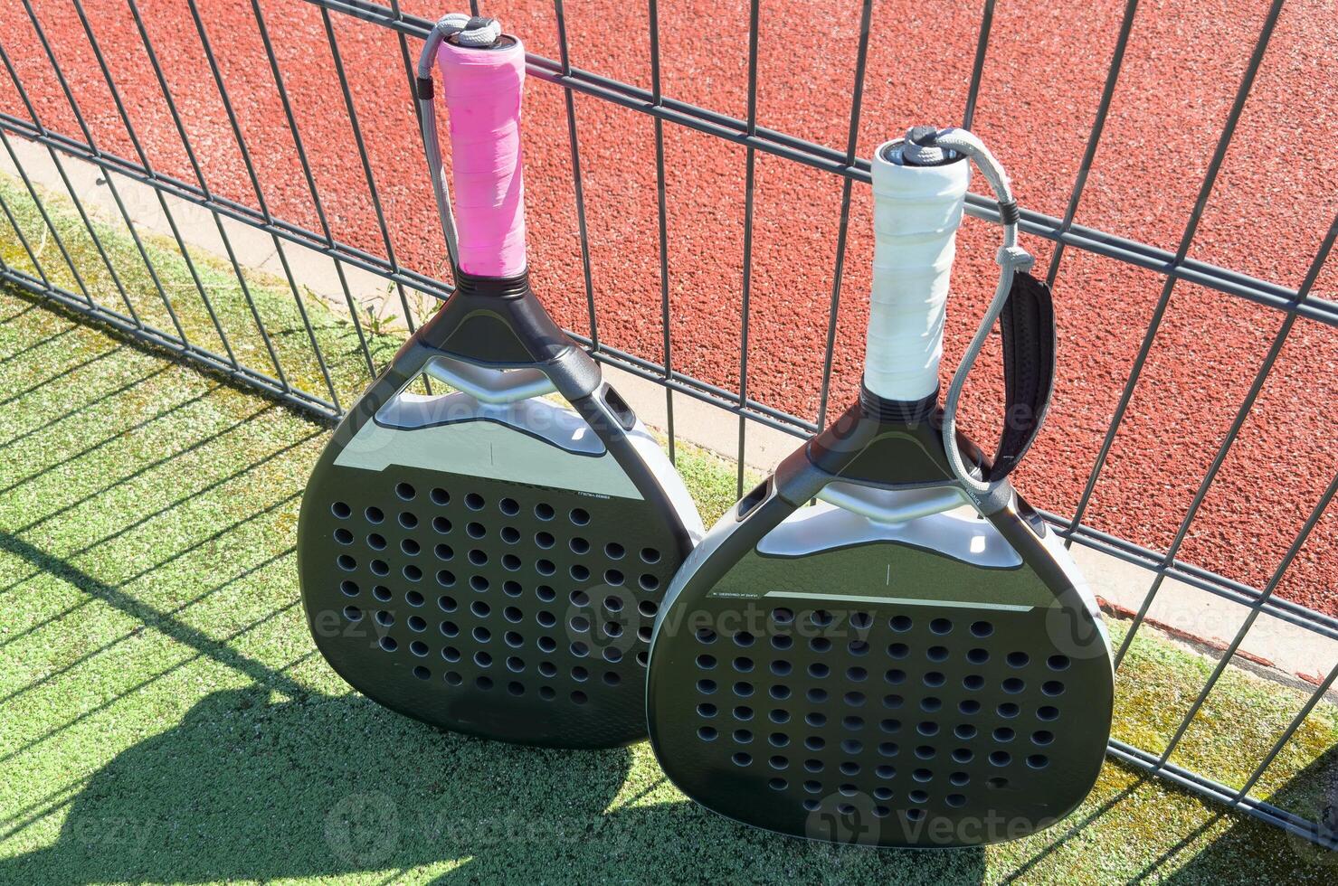 Padel racket and yellow ball behind net on a green court grass turf outdoors. Paddle is a racquet game. Professional sport concept with space for text photo