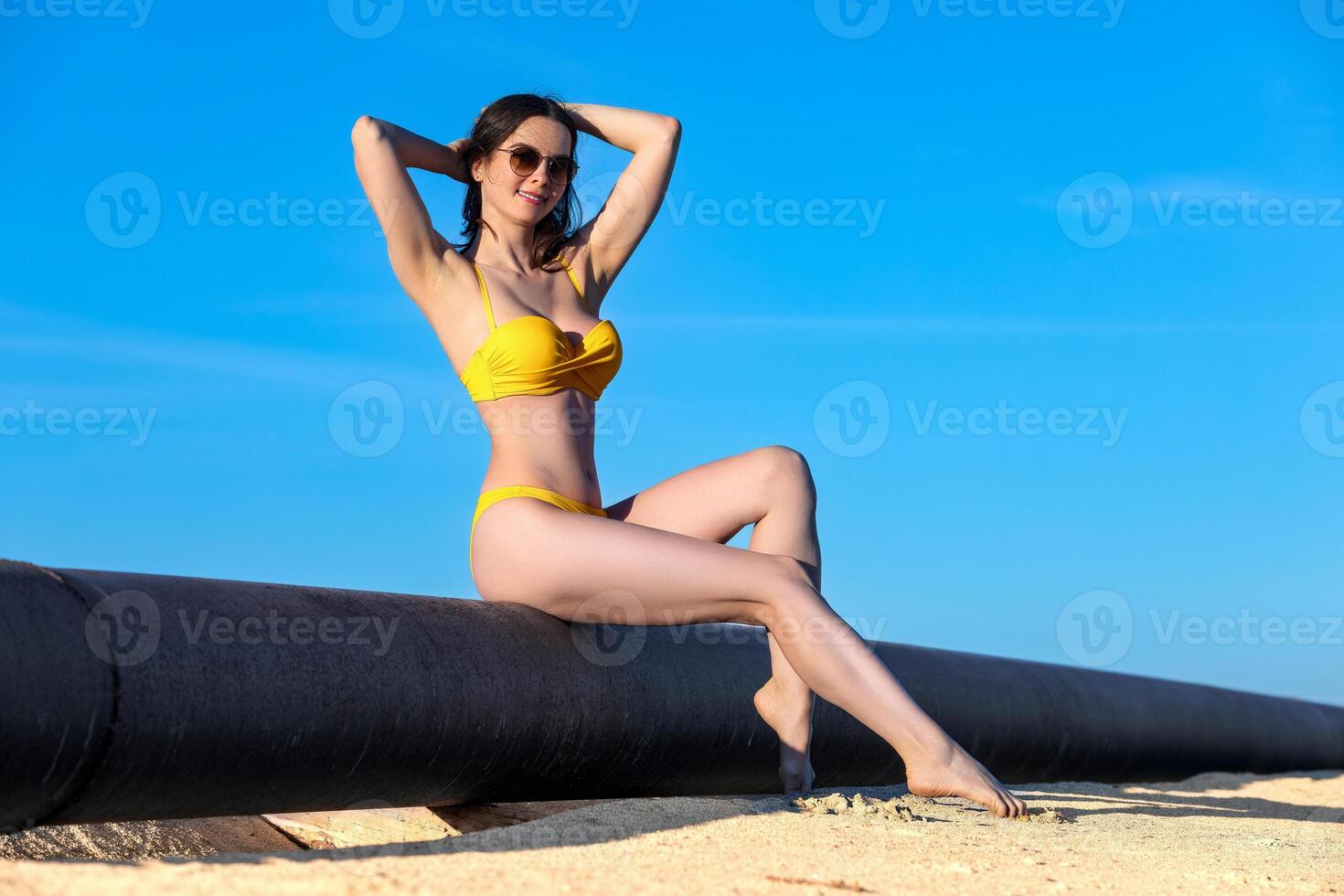 Beautiful young woman in a yellow swimsuit and sunglasses on the beach photo