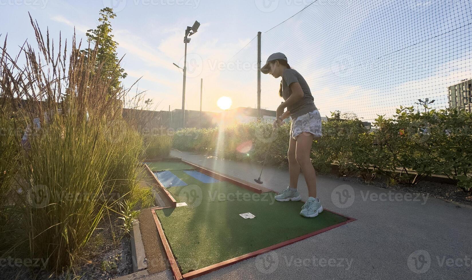 Mini Golf - girl playing Golf on green grass at sunset photo