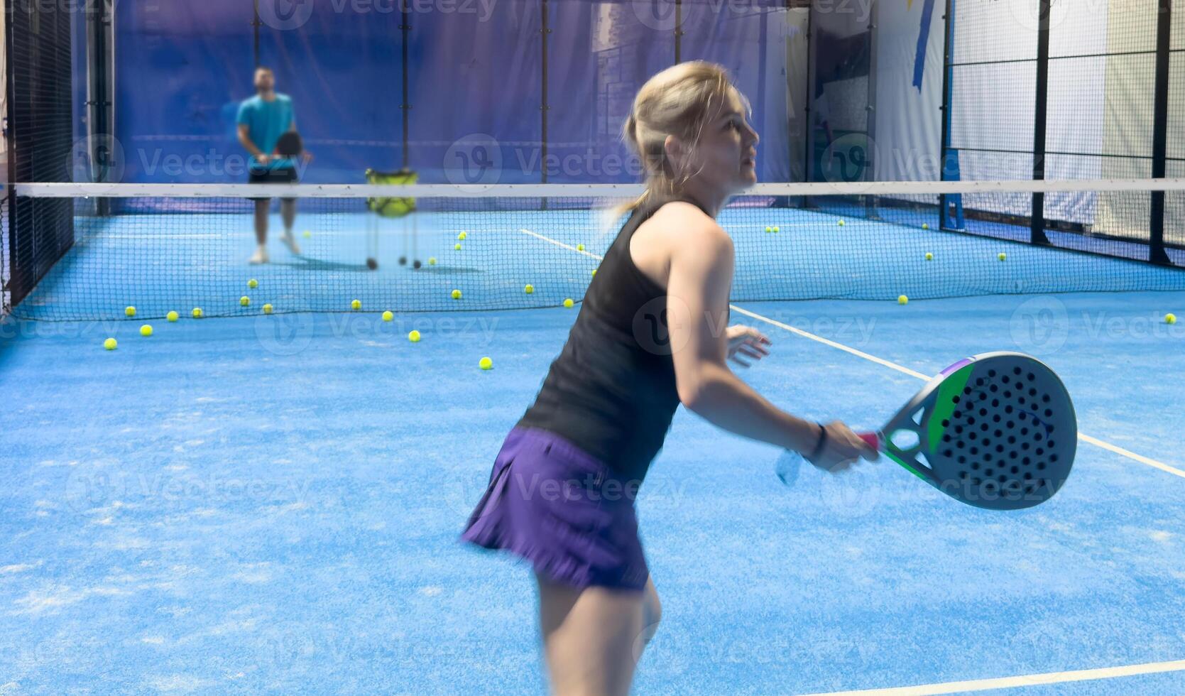 A woman is playing padel, hitting a ball on a bright blue court, photo