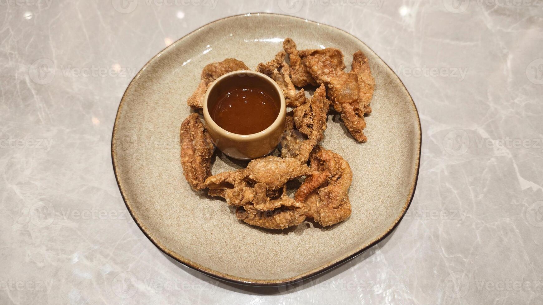 Close-Up of Crispy Fried Chicken Skin with Dipping Sauce on a Brown Plate with Marble Background in a Restaurant photo