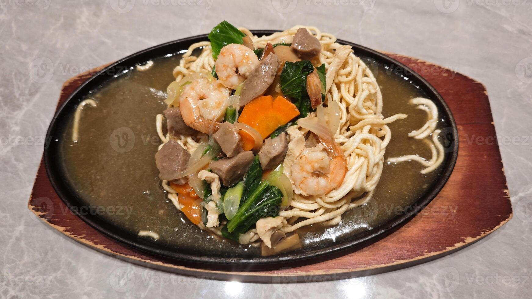 Hot Plate Noodle with Capcay Vegetables and Shrimp on Marble Table in a Restaurant photo