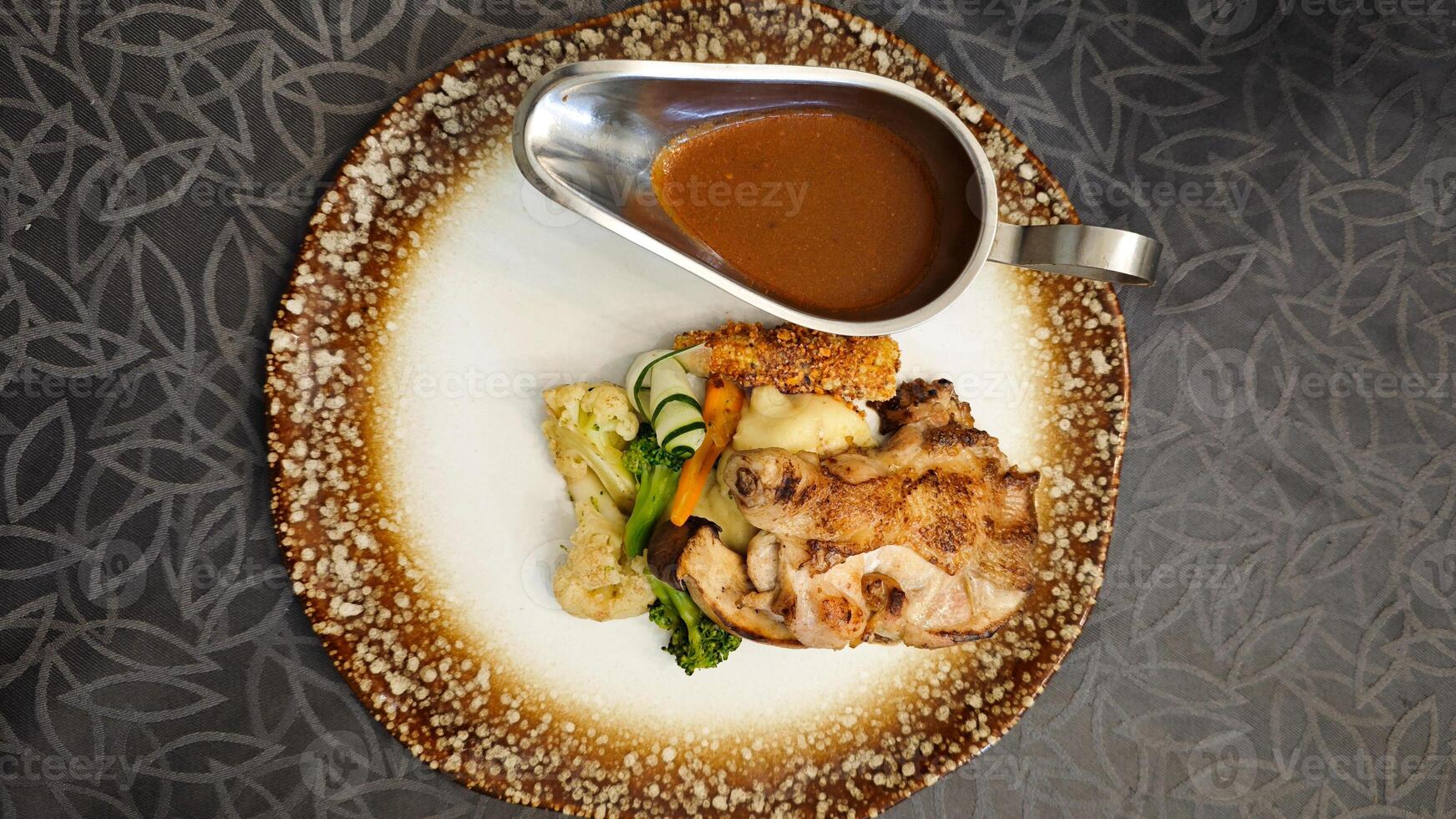 Lavish Chicken Steak Meal with Vegetables and Sauce on a Decorative Plate with Dark Patterned Background photo