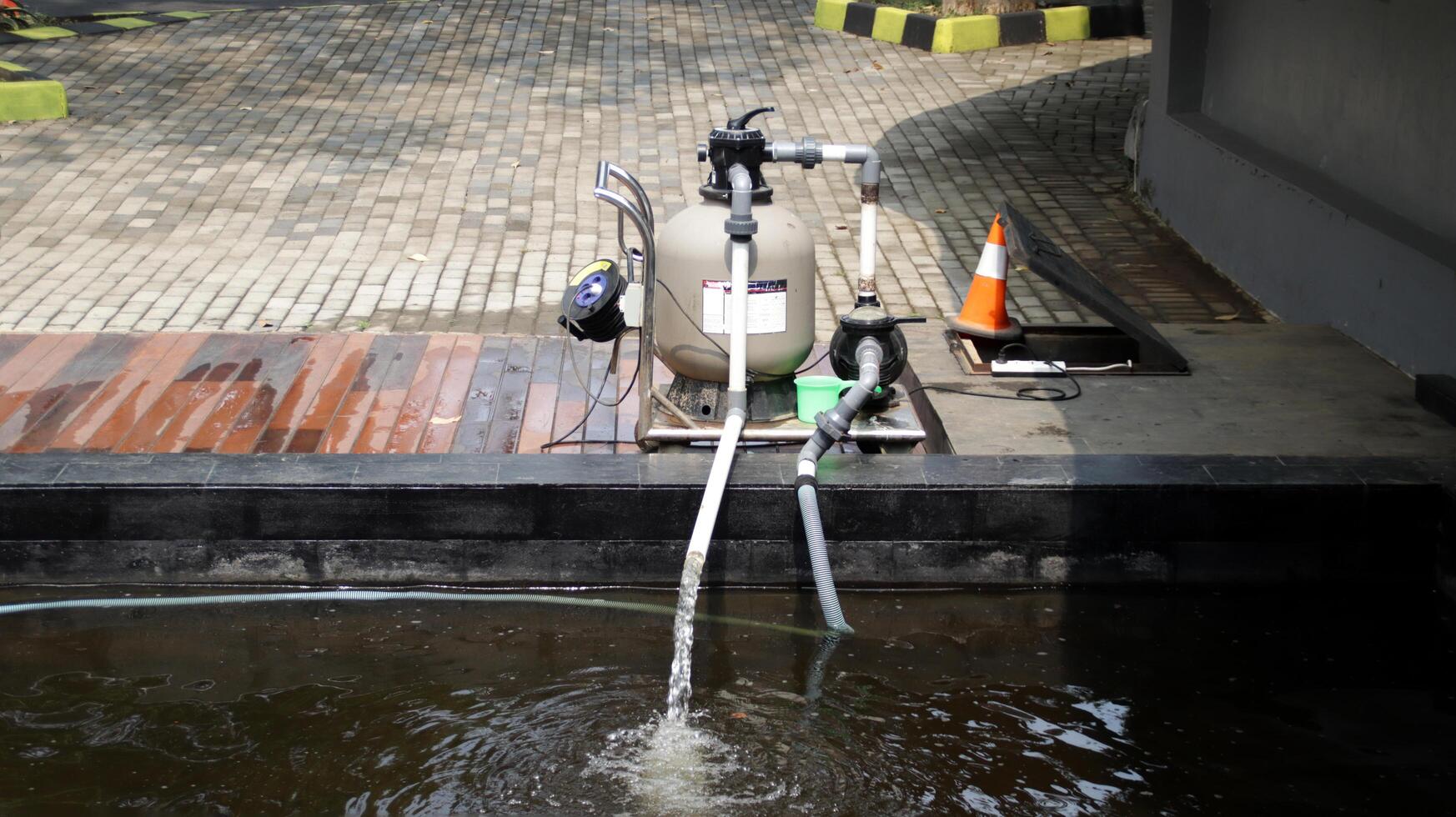 Outdoor Water Pump System Filtering Pond Water with Orange Safety Cone and Brick Pathway Background in Bright Daylight photo