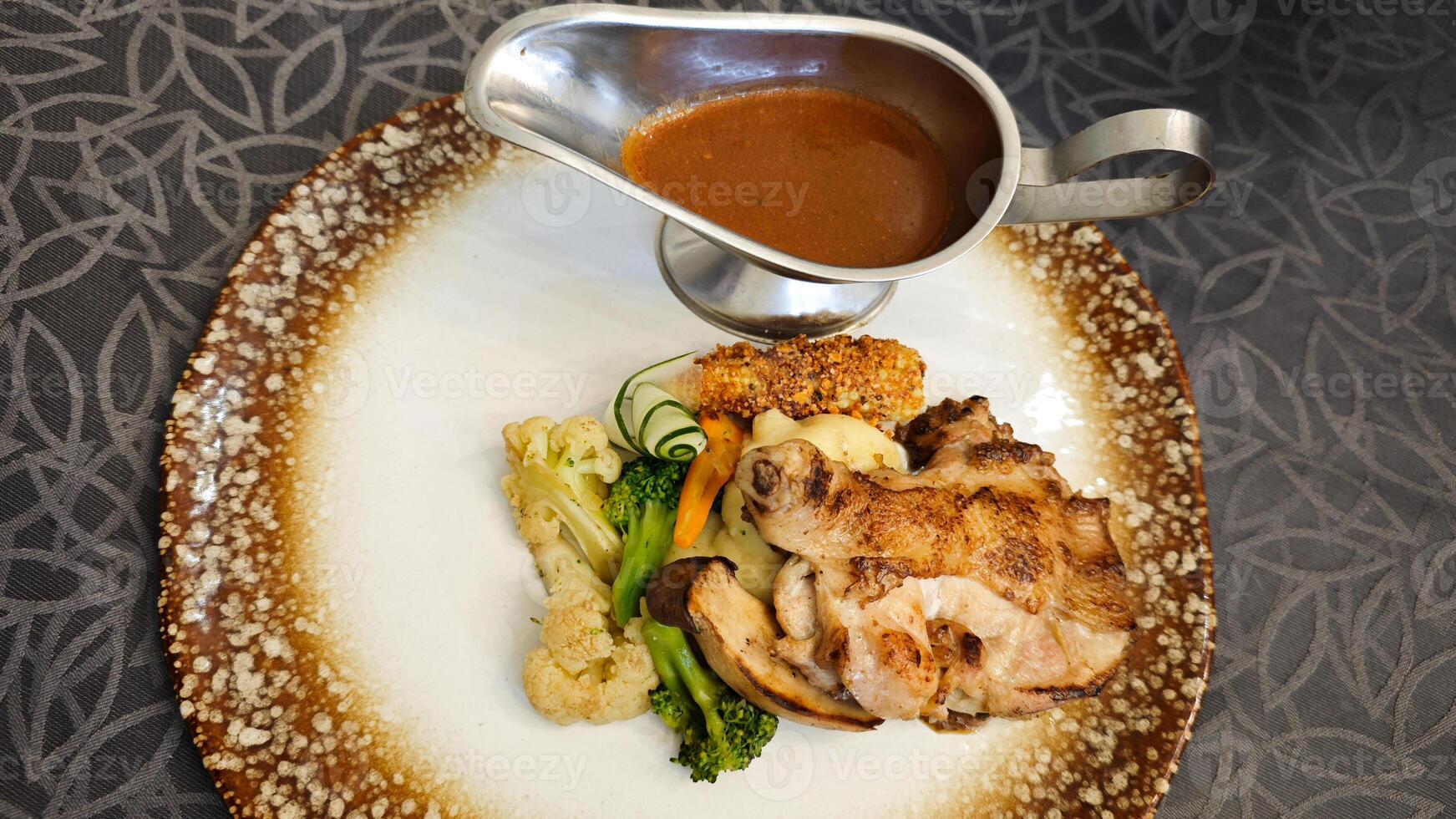 Lavish Chicken Steak Meal with Vegetables and Sauce on a Decorative Plate with Dark Patterned Background photo