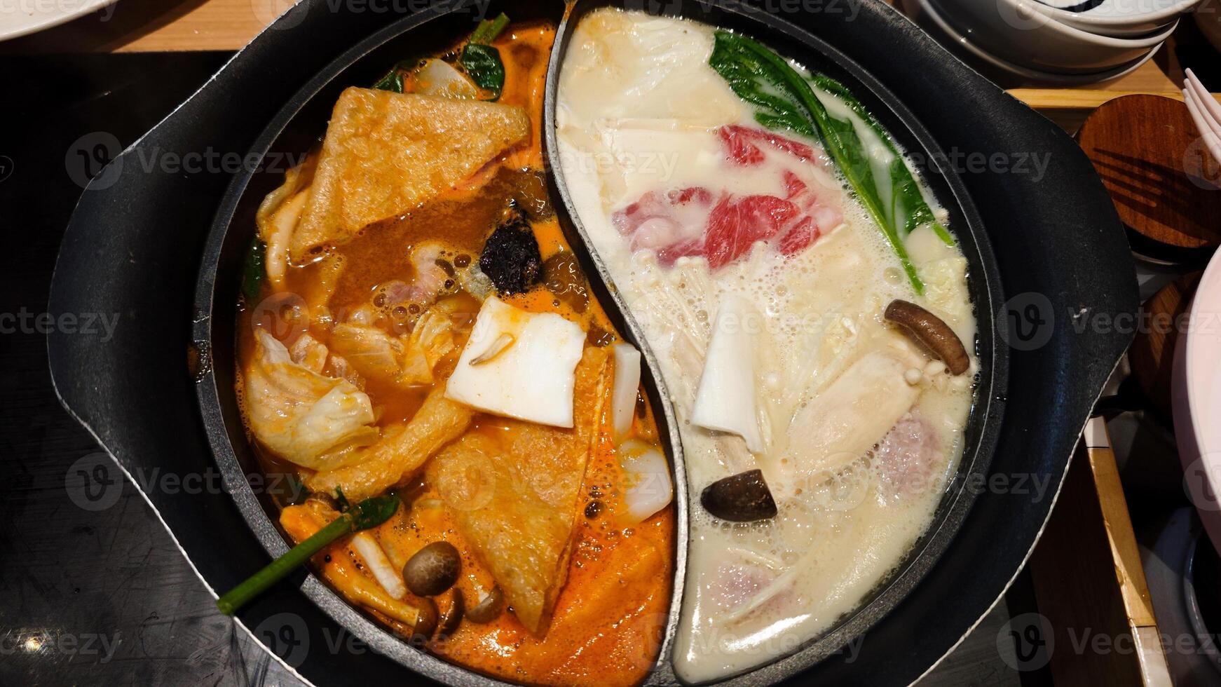 Dual Flavor Hot Pot with Spicy and Regular Broth Featuring Fresh Vegetables and Meats in a Restaurant Setting photo