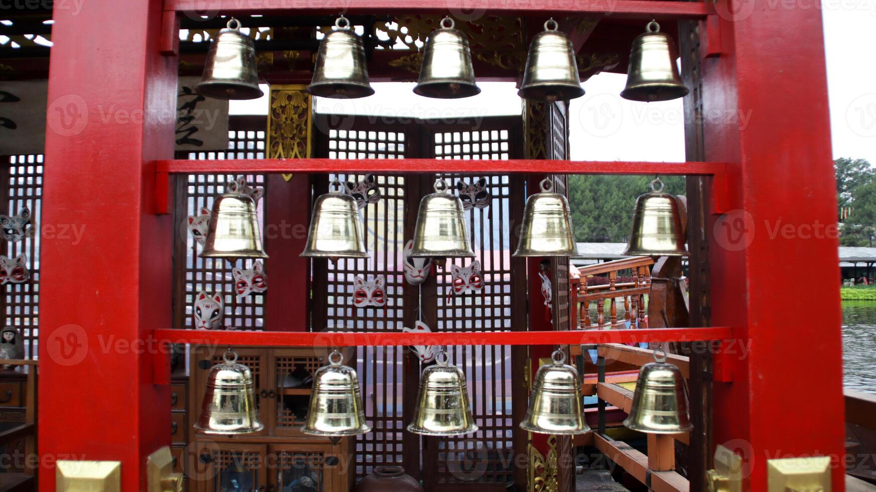 Row of Golden Bells Hanging on Red Wooden Frame in Traditional Cultural Setting with Decorative Masks photo