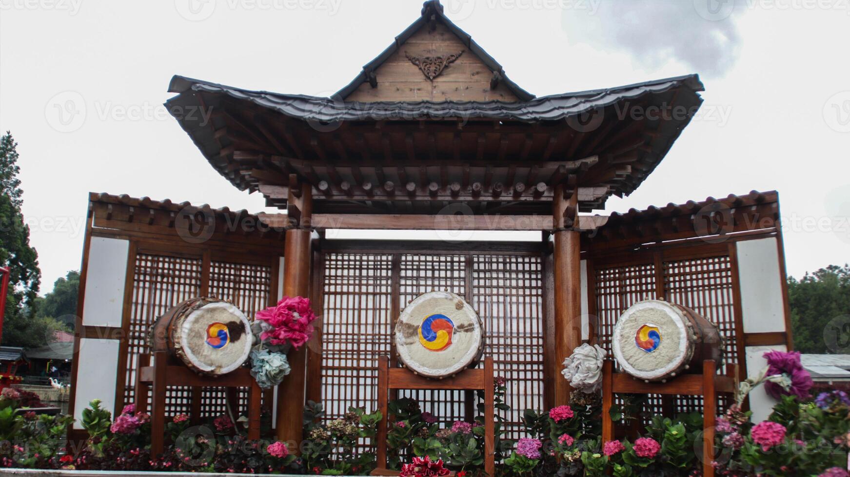 Traditional Korean Pavilion with Colorful Drums and Lattice Background Surrounded by Vibrant Flowers photo